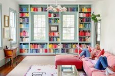 51 a colorful living room with blue bookshelves and colorful books, a coral L-shaped sofa, a glass coffee table and a chandelier