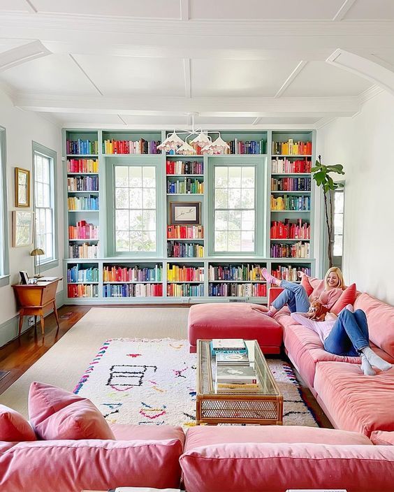a colorful living room with blue bookshelves and colorful books, a coral L-shaped sofa, a glass coffee table and a chandelier