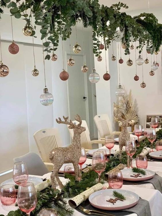 a Christmas tablescape with an evergreen runner and greenery and ornaments hanging over the table