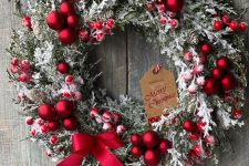 a beatiful frozen Christmas wreath with red ornaments, berries, a red bow and a tag is a gorgeous decor idea