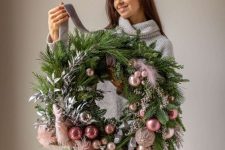 a beautiful and lush Christmas wreath of evergreens and leaves, pink and peachy pink ornaments and feathers is a whimsy solution