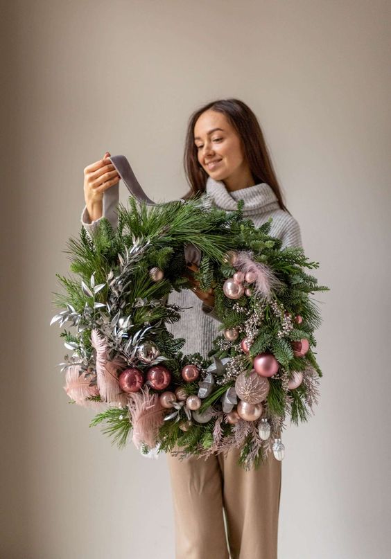 a beautiful and lush Christmas wreath of evergreens and leaves, pink and peachy pink ornaments and feathers is a whimsy solution