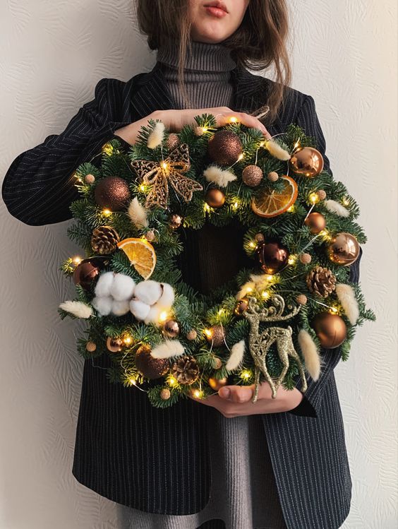 a beautiful holiday wreath of evergreens, brown ornaments, pinecones, citrus, cotton and lights is wow