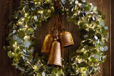 a beautiful vintage-inspired greenery wreath with lights and large vintage bells is a stylish holiday decoration