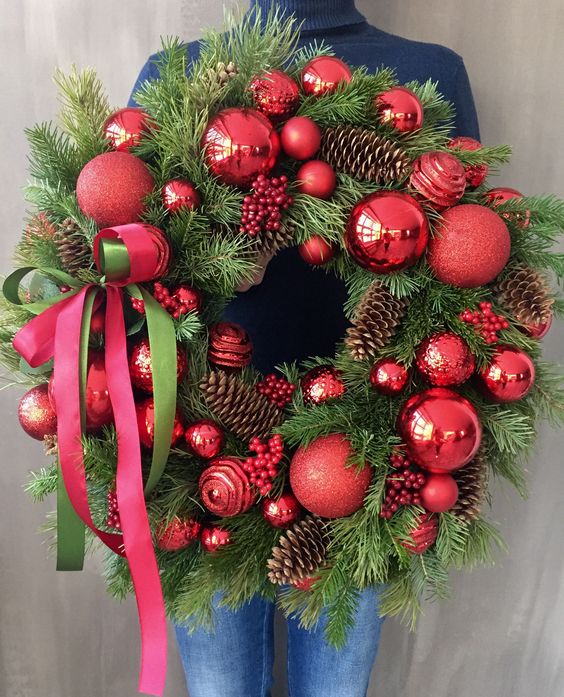 a bold and catchy Christmas wreath of evergreens, pinecones, red ornaments and a red bow is a cool and brigth decor idea