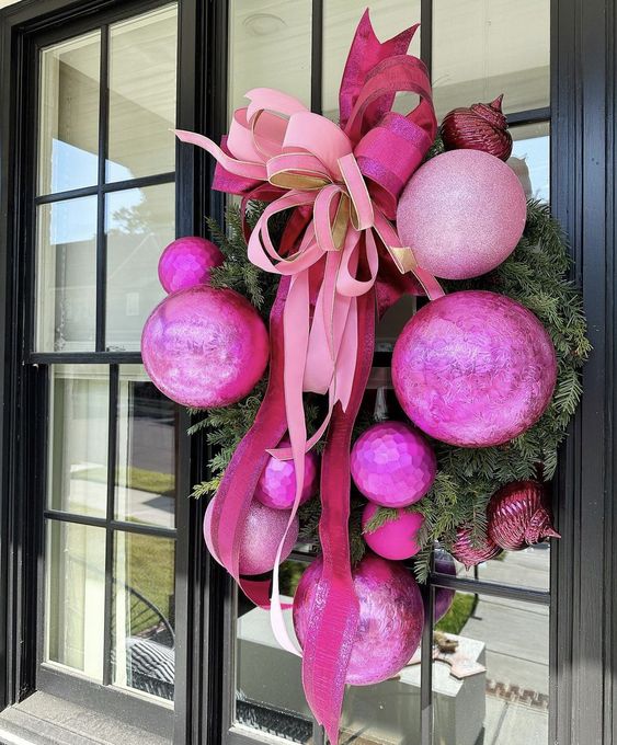 a catchy holiday wreath of evergreens and oversized pink ornaments plus a big bow on top is amazing