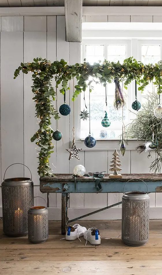 a cool Christmas ornament display covered with greenery and lights and with various green and blue ornaments is a lovely idea