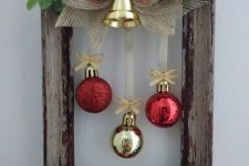 a cute frame Christmas wreath with red and gold ornaments, a gold bell on top, eucalyptus, leaves and a red bow is lovely