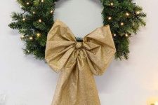 a glam evergreen Christmas wreath with lights and a gold glitter bow is a cool idea to realize