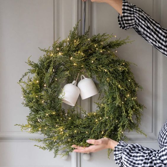 a greenery Christmas wreath with lights and large white bells looks fresh and up-to-date