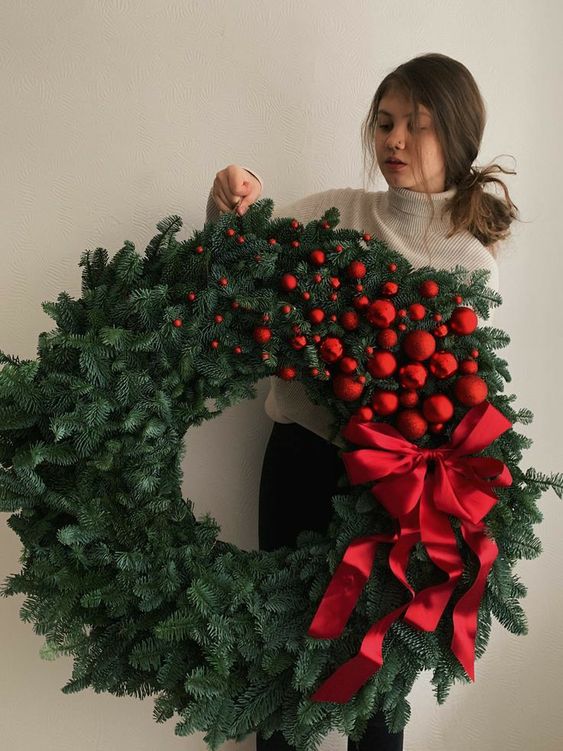 a jaw-dropping evergreen Christmas wreath with small and large red ornaments and a large red bow is amazing