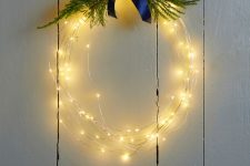 a light wreath topped with greenery and a navy ribbon bow on top is a cool and cute holiday decoration