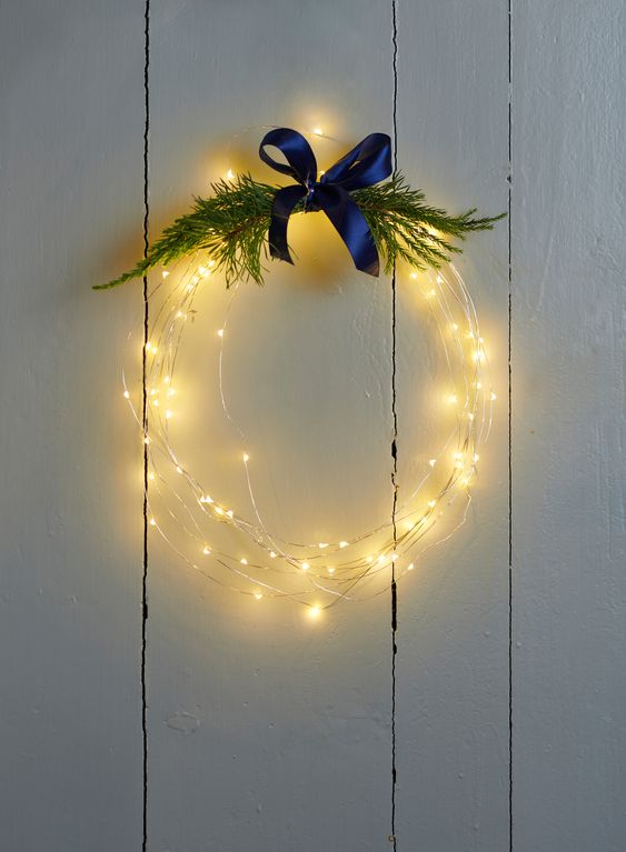a light wreath topped with greenery and a navy ribbon bow on top is a cool and cute holiday decoration