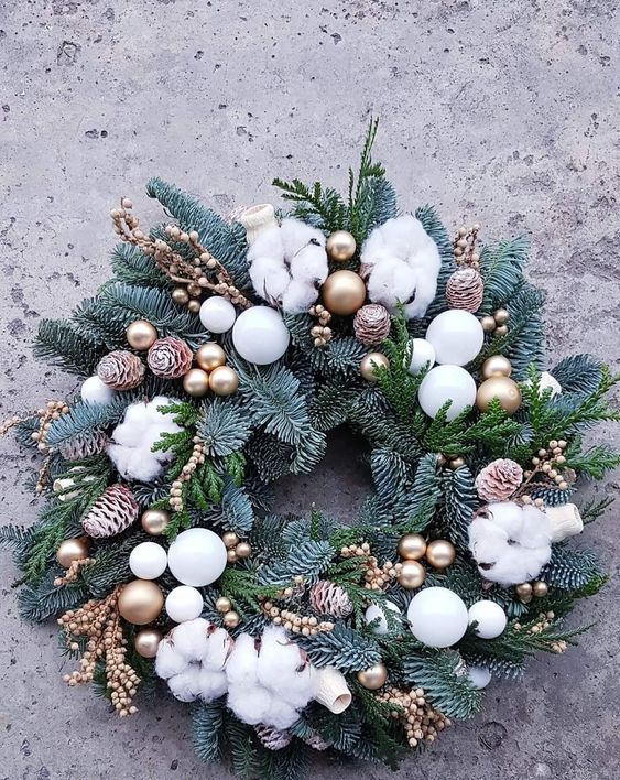 a lovely Christmas wreath of evergreens, berries, pinecones, gold and white ornaments and cotton is chic