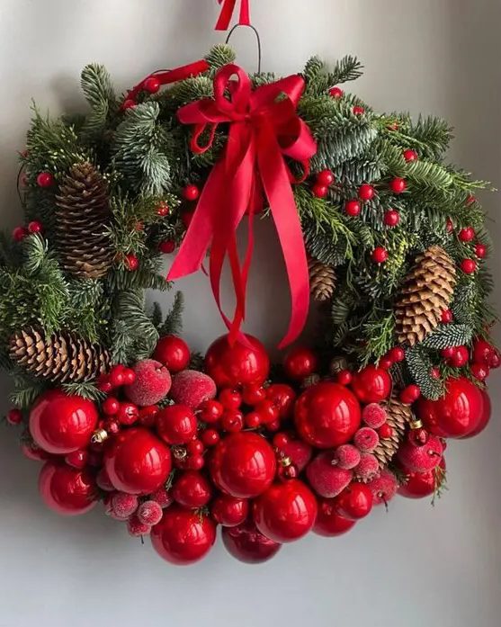 a lovely Christmas wreath of evergreens, cranberries, red ornaments and sugared apples, pinecones and a large red bow on top is a bold and cool idea