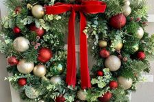 a lovely greenery holiday wreath with evergreens, gold, red and green ornaments and a red bow is a stylish decoration