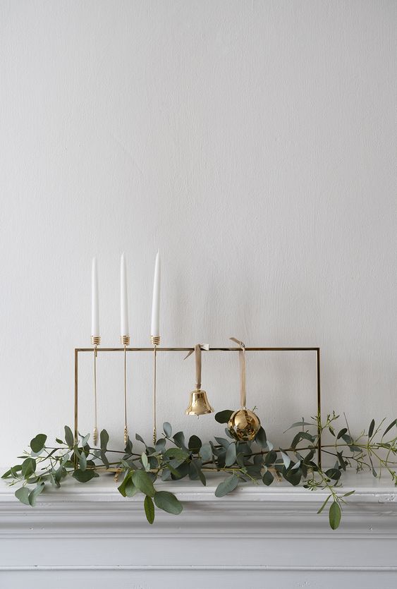 a minimal frame with a bell and an ornament, some greenery and candles in tall gold candleholders