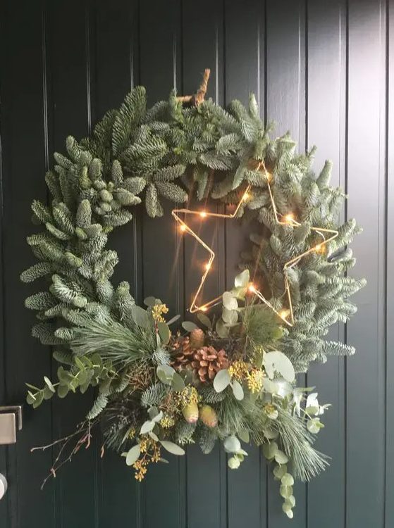 a modern Christmas wreath of evergreens, twigs, greenery, pinecones and a lit up star is a cool and catchy idea
