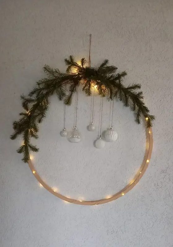 a modern Christmas wreath with lights, evergreens, white ornaments hanging down is a lovely idea for winter decor