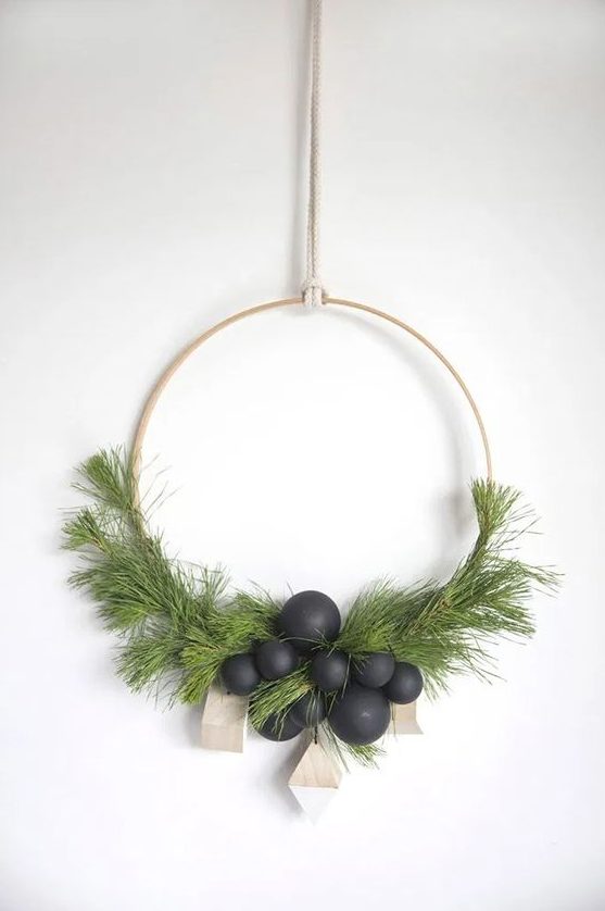 a modern Scandinavian Christmas wreath with evergreens, matte black ornaments and wooden geometric ornaments is wow