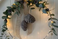 a rustic Christmas wreath with lights, greenery, pinecones and a burlap bow is amazing