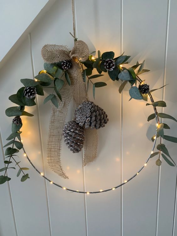 a rustic Christmas wreath with lights, greenery, pinecones and a burlap bow is amazing