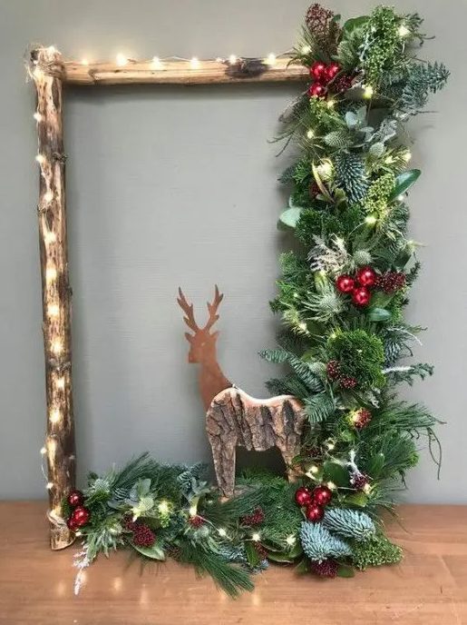 a rustic frame Christmas wreath with lights, evergreens, leaves, a wooden deer, berries and pinecones