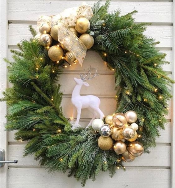 a stylish evergreen holiday wreath with gold ornaments, lights and a single white deer inside