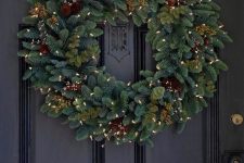 a stylish evergreen wreath with pinecones, berries and lights is a cozy idea for the holidays
