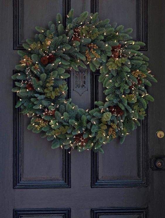a stylish evergreen wreath with pinecones, berries and lights is a cozy idea for the holidays