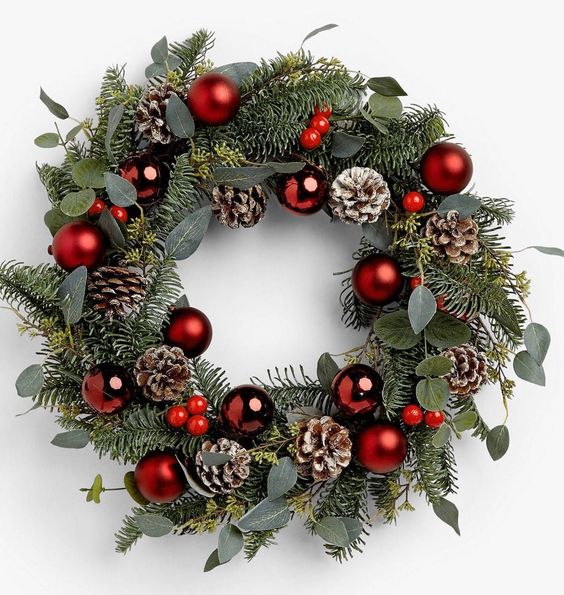 a stylish holiday wreath of evergreens and eucalyptus, red ornaments, snowy pinecones and red berries
