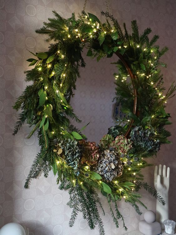 a textural Christmas wreath with evergreens, greenery, lights and blooms is a stylish decor idea