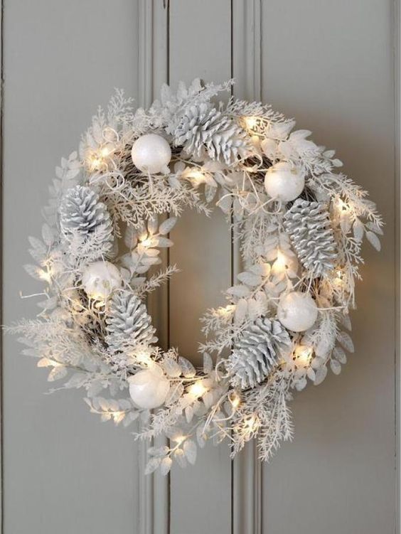 a white Christmas wreath with pinecones, leaves, ornaments and lights for an all-neutral or winter wonderland space