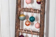 a wooden ladder with colorful Christmas ornaments hanging is a cool and catchy decor idea