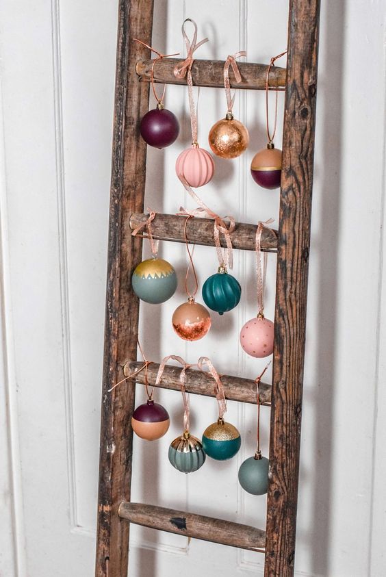a wooden ladder with colorful Christmas ornaments hanging is a cool and catchy decor idea