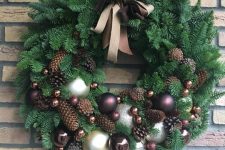 an elegant evergreen Christmas wreath with silver and brown ornaments, pinecones and a ribbon bow is chic and cool