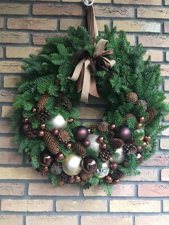 an elegant evergreen Christmas wreath with silver and brown ornaments, pinecones and a ribbon bow is chic and cool