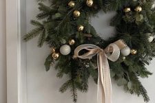 an elegant evergreen and eucalyptus Christmas wreath with white and gold ornaments and a tan ribbon bow looks cool