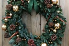 an evergreen Christmas wreath with gold ornaments, cinnamon, little brown ornaments, pinecones and a green bow