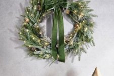 an evergreen Christmas wreath with pinecones and lights plus a green bow is a glam and chic idea