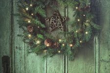 an evergreen Christmas wreath with pinecones and lights plus a twig star is a cool rustic decoration for the holidays