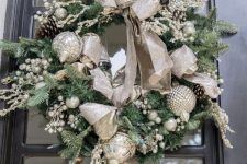 an evergreen holiday wreath with glam silver ornaments and a large silver ribbon bow, silver berries and some pinecones