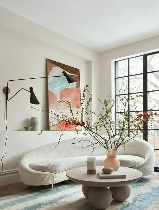 a beautiful living room with a curved creamy sofa, a round coffee table, a bold artwork, black wall lamps and a glazed wall