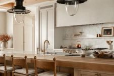 03 a beautiful earthy kitchen with white cabinets and a built-in hood, a large stained kitchen island, vintage pendant laps
