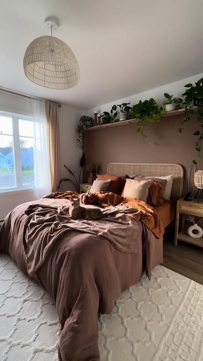 an earthy bedroom with a brown accent wall, a bed with a cane headboard, brown and rust bedding, potted greenery