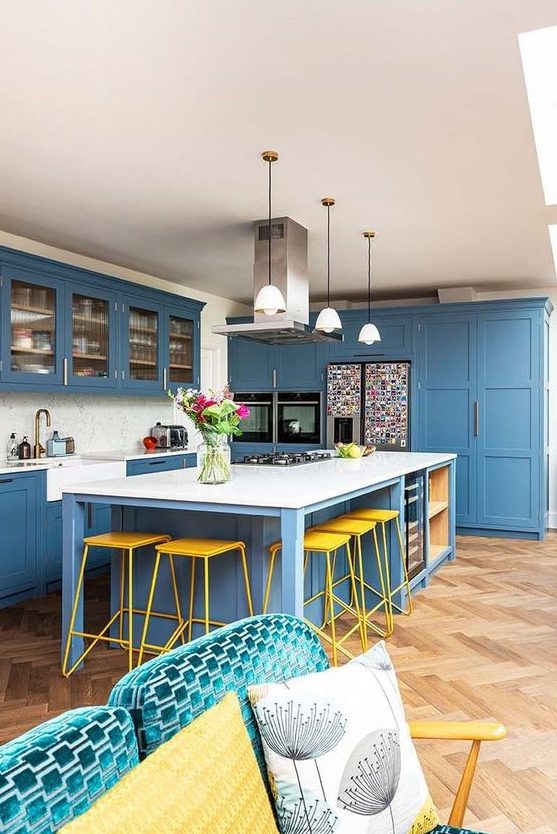 a bright and stylish coastal kitchen done in blue, with white countertops and a backsplash, pendant lamps and a sofa with pillows