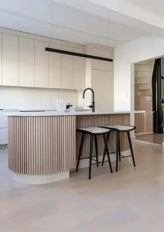 a minimal tan kitchen with matte plain cabinets, a matching backsplash and a ribbed kitchen island with a black faucet as an accent