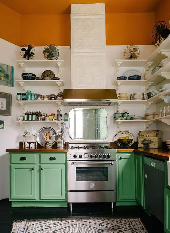 a bold kitchen with color block white and rust wall, green cabinets, stainless steel appliances and a patterned hood