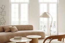 08 a neutral living room with a curved tan sofa, round coffee tables, a curved rattan, floor lamp and a neutral rug
