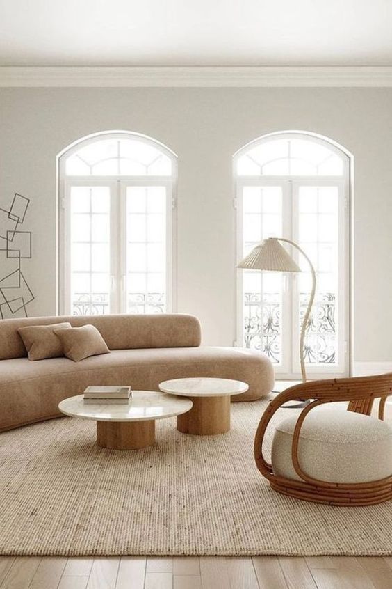 a neutral living room with a curved tan sofa, round coffee tables, a curved rattan, floor lamp and a neutral rug